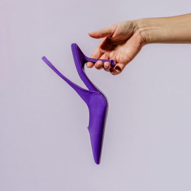 hand holding purple high heel pump on lavender background