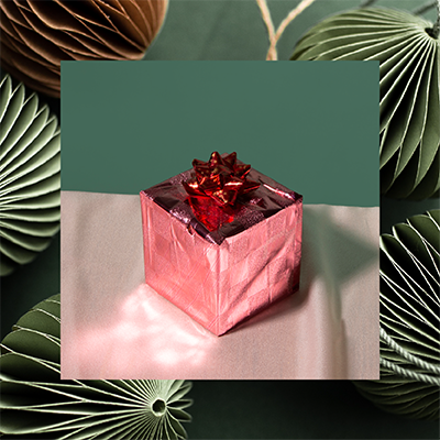 JLL_52538_F9b_ContactUs_PNG_1mb_400sq_01kk Pink foil wrapped present with paper ornaments in background